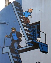 Photographie du mur de pignon d'un immeuble entièrement peint, figurant Tintin, le capitaine Haddock et Milou descendant un escalier extérieur.