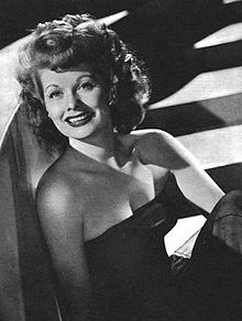 Glamorous publicity shot of Lucille Ball from the waist up, dressed in a blue strapless gown and smiling.