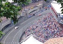Photo d'une route avec deux monoplaces de Formule 1. À droite, des gradins avec du public