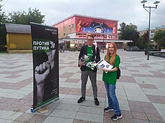 Photographie en couleurs d'un homme et une femme portant des T-shirts verts et distribuant des tracts en ville.