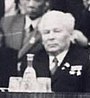 A elderly man, balding with white hair, in a suit