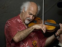 A man wearing a red printed shirt, playing the fiddle