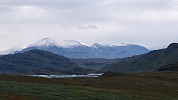 Photographie en couleurs de massifs montagneux et de roches affleurantes entourant les eaux d'un fjord.