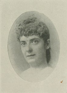 B&W oval portrait photo of a woman with her hair in an. up-do, wearing a white blouse.