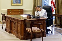 Barack Obama on the phone while sitting at the Resolute desk in 2009. The wooden box holding the button is visible next to the phone.