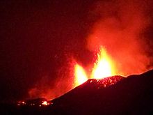 Two glowing fountains of lava sending blobs of volcanic material out the summit of a volcano.