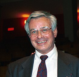 Photographie en couleurs d'un homme au visage souriant, et aux cheveux gris argentés.