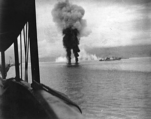 Japanilainen lentokone savuaa alasampumisen jälkeen Guadalcanalilla 12. marraskuuta 1942. Taustalla aseistettu rahtialus USS Betelgeuse.