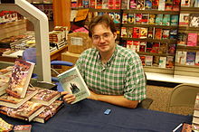 Foto von Brandon Sanderson hält bei einer Signierstunde die deutsche Ausgabe von Elantris in die Kamera