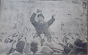 Photographie de presse en noir et blanc montrant un homme soulevé par la foule et entouré de ballons.