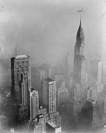 Many buildings and skyscrapers seen from a great height, surrounded by smog. Unlike the previous image above, no horizon can be seen as the entire sky is blotted out by the smog. If the position of the prior photo was "above" a blanket of smog, this photo is completely underneath and within it.