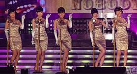 Пять женщин с прической как улей, одетых в золотые платья-футляры и перчатки до локтя