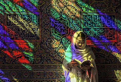 Žena čtoucí ve světle vitráží mešity Násir al Mulk v íránském Šírázu