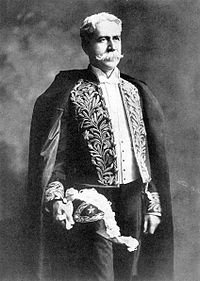 Photograph showing the head and shoulders of an older man with large sideburns and wearing a formal coat and black bow tie