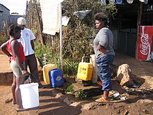 A group of people gathering around a communal tap in Johannesburg, South Africa Communal tap for drinking water (2941731238).jpg