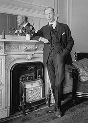 Black and white photo of Prokofiev standing beside a fireplace, his arm resting on the mantlepiece