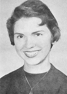 Black and white head and shoulders of a short-haired woman in a dark blouse wearing a drop necklace