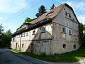 Wassermühlenanwesen mit Wohnhaus (Umgebinde) über Hakengrundriss, Gartenlaube und schmiedeeiserner Einfriedung sowie gegenüberliegendem Mühlengebäude (Nr. 14a) mit Esse, vorhandenem Wasserbau und Technik