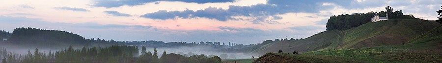 Vallée avec de la brume dominée par des collines, avec à droite l'église.