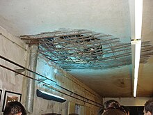 Бетонный потолок с пробитым большим отверстием, в котором видны арматурные металлические стержни, встроенные в бетон.