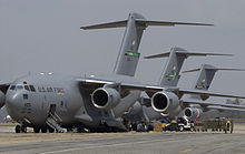 Vehicles and personnel unloading supplies from three gray C-17s parked together for victims of Hurricane Katrina.