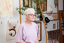 Une femme âgée devant des dessins accrochés au mur