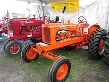 Two tractors on display in a tent. In the rear, a red one labeled "McCORMICK FARMALL". In front is an orange one, labeled ALLIS-CHALMERS with a "WD 45" emblem. A banner behind them reads CNY Two-Cylinder Club"