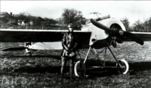 Photo noir et blanc de mauvaise qualité d'un homme en tenue de vol devant un avion monoplan.