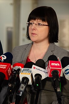 Photo of Kaja Godek in 2019; wearing mid-length hair, glasses without rim, grey suit jacket