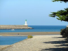 Vue d’une jetée, surmontée d’un phare, à partir d’une plage.