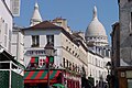 Ei gate på Montmartre med eit par av kuplane på katedralen Basilique du Sacré-Cœur de Montmartre stikkande opp i bakgrunnen.