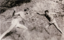 Фотография двух подростков, изображенных в оттенках сепии, изображающих драку, один слева держит палку вместо копья.