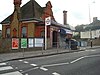 A brown-and-red bricked building with a rectangular, dark blue sign reading "WIMBLEDON PARK STATION" in white letters all under a blue sky