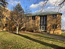 Photograph of a two-story building with a tan brick facade and green copper roofing. A few steps lead up to wide glass doors. Signage above the doors reads "ELECTRONICS LABORATORY"