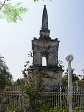 Tall stone memorial with spire and surrounded by a metal fence.