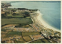 Photo aérienne montrant le littoral d'une plage. Les champs attenants sont remplis de tentes de camping.