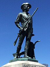 Greened bronze statue of a young colonial man. He holds a rifle, and his coat is on a plow beside him.