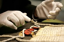 A manuscript and seals being examined at the archives A gloved pair of hands at The National Archives.jpg