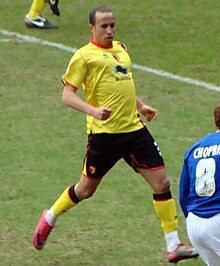 A young man, wearing a yellow top, standing on a grass field.