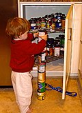 Young boy stacking a seventh can atop a column of six food cans on the kitchen floor. Repetitively stacking or lining up objects is a behavior sometimes associated with individuals with autism.