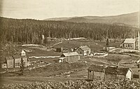 Den nye Hattfjelldal kirke under bygging i 1868 ytterst til høyre i bildet. Til venstre sees den gamle kirken som ble revet i 1874. Denne kirken var bygget i 1788 og var den andre på stedet. Foto: Ukjent / Riksantikvaren