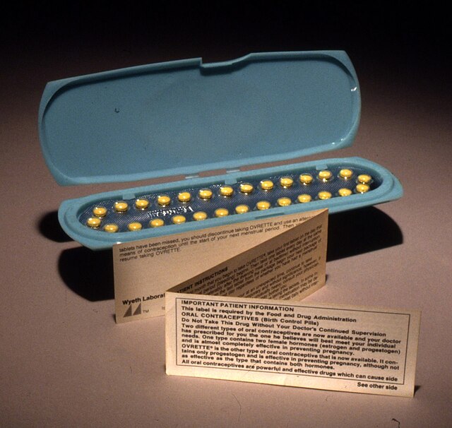An oblong blue container holding 28 yellow pills, with a small, folded paper note standing in front of it