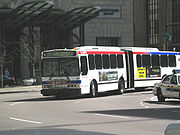 Белый автобус из двух секций, соединенных черным компенсатором, уходит в поворот.