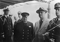 Photographie en noir et blanc représentant deux hommes entourés de militaires vêtus d'uniformes sombres.