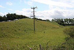 A green filed with a steep long mound in the middle