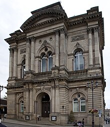 Die frontale Sicht auf die Town Hall im klassizistischen Baustil mit Säulen und Reliefen und einer aufsteigenden Treppe zum dunklen Portal.