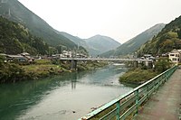 Photo couleur d'un pont suspendu au-dessus d'une rivière sur fond de paysage de montagne.
