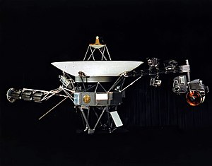 A space probe with squat cylindrical body topped by a large parabolic radio antenna dish pointing upwards, a three-element radioisotope thermoelectric generator on a boom extending left, and scientific instruments on a boom extending right. A golden disk is fixed to the body.