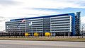 A wide rectilinear six-story blue-and-white building with the American, Canadian and Mexican flags flying in front, seen from a nearby roadway, under a cloudy sky