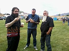 Bo Huff stands with two car show participants on a grassy field with cars in the background